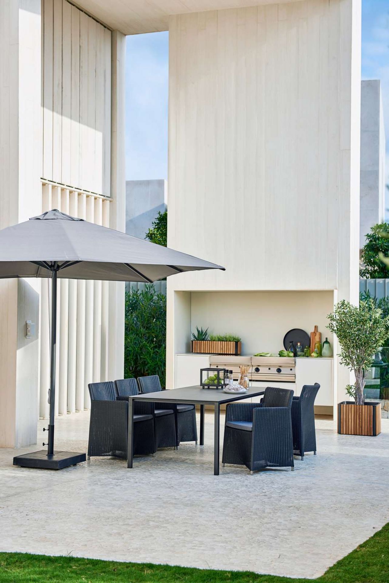 Cane-Line Diamond Outdoor Stuhl: Schwarzer Rattan Gartenstuhl mit Armlehne und grauen Sitzkissen auf Terrasse.