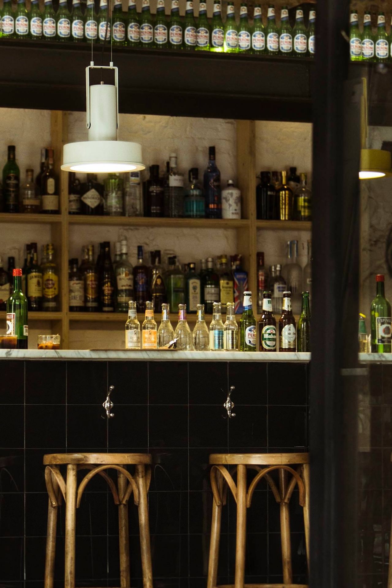 Arne Domus Hängeleuchte von Santa & Cole über Bar mit Flaschen und Hockern.