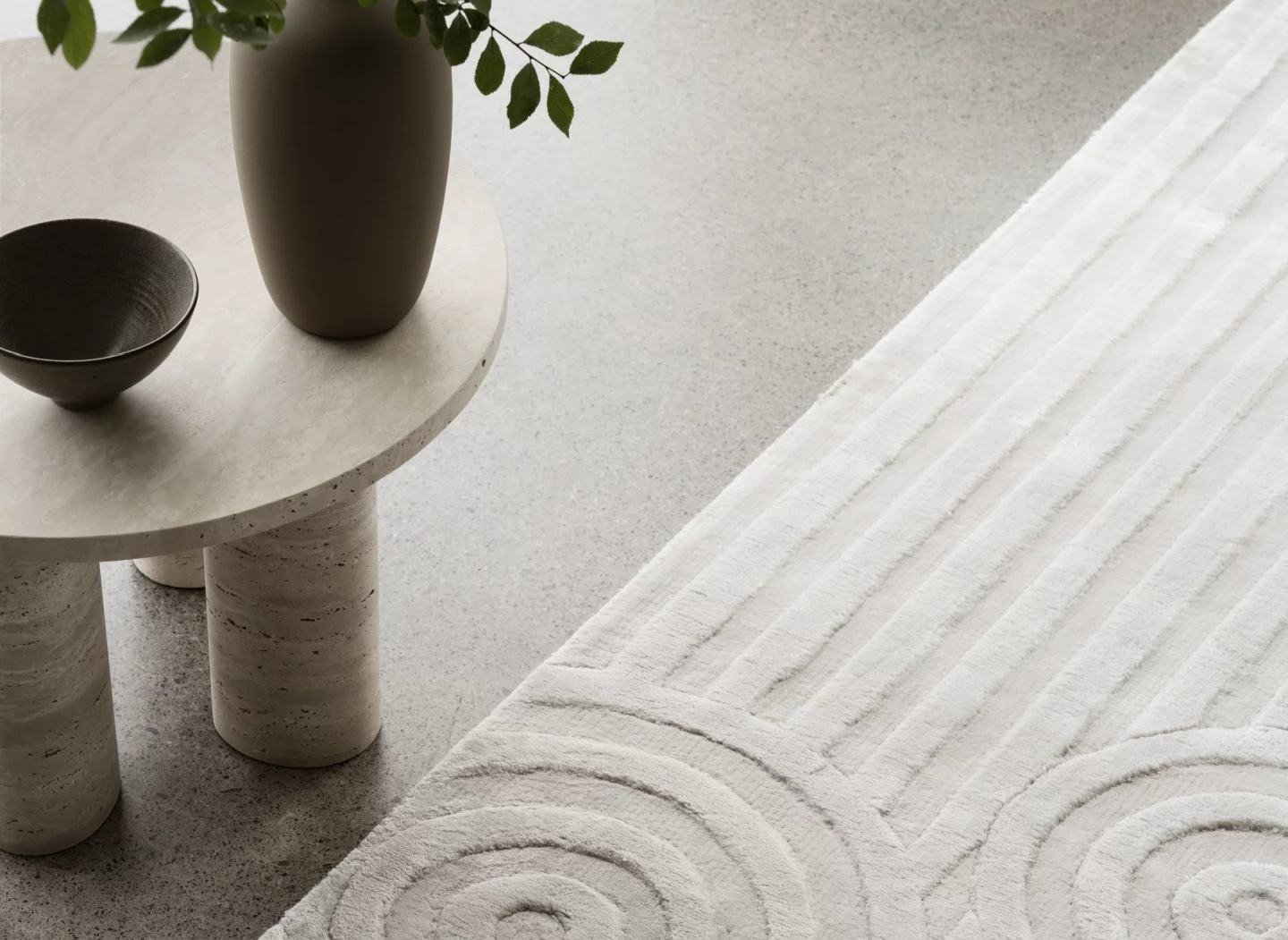 Detailaufnahme des Blomus Uzu Rug Teppichs in Beige mit geometrischem Muster neben einem Beistelltisch.