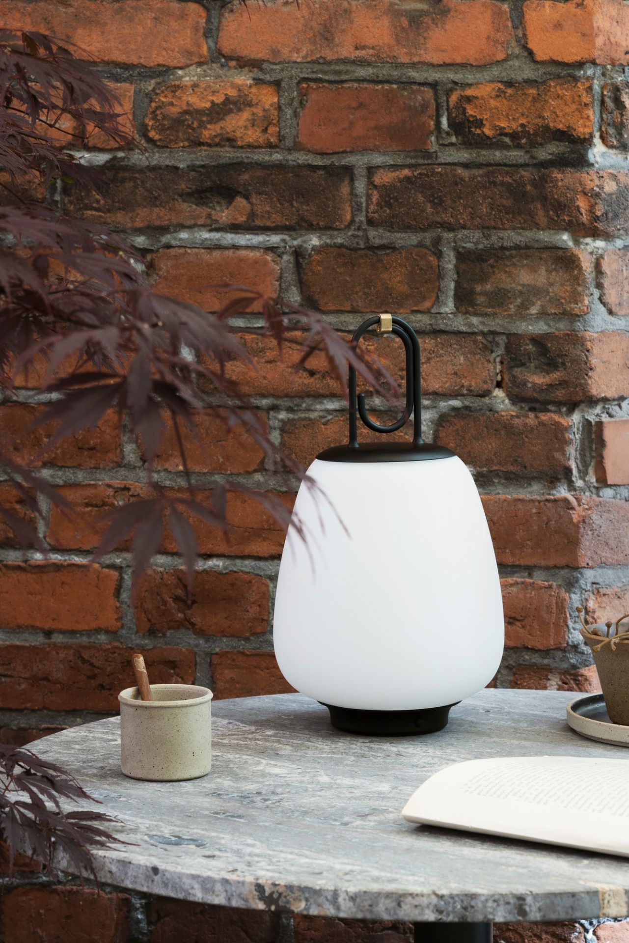 Lucca Akkuleuchte schwarz von AndTradition auf Tisch, stimmungsvolle Beleuchtung für drinnen und draußen.