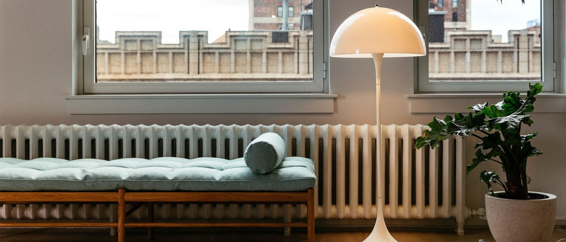 Helle Panthella Stehleuchte von Louis Poulsen neben Bank und Zimmerpflanze, modernes Wohnzimmer Design.