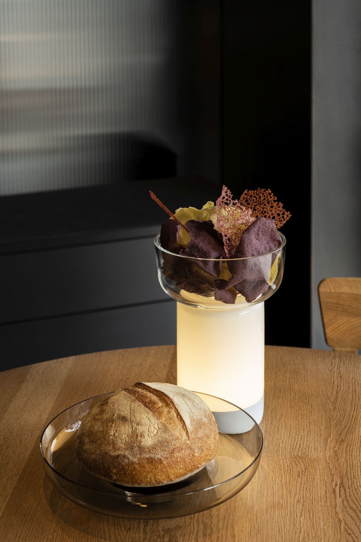 Bontà Akkuleuchte von Artemide: Tischleuchte mit Topas-farbener Platte und Speisen in Glasschale.