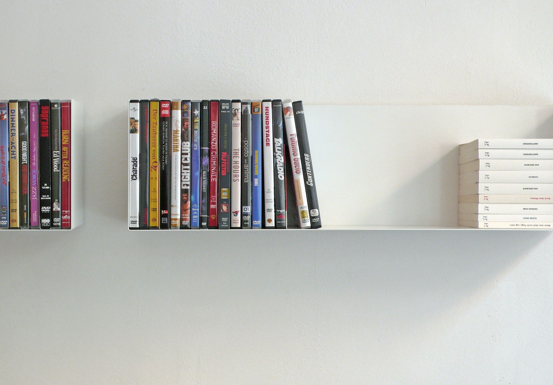 Weißes Wandregal a Linea1 von Müller Möbelwerkstätten mit DVDs und Büchern, minimalistisches Design.