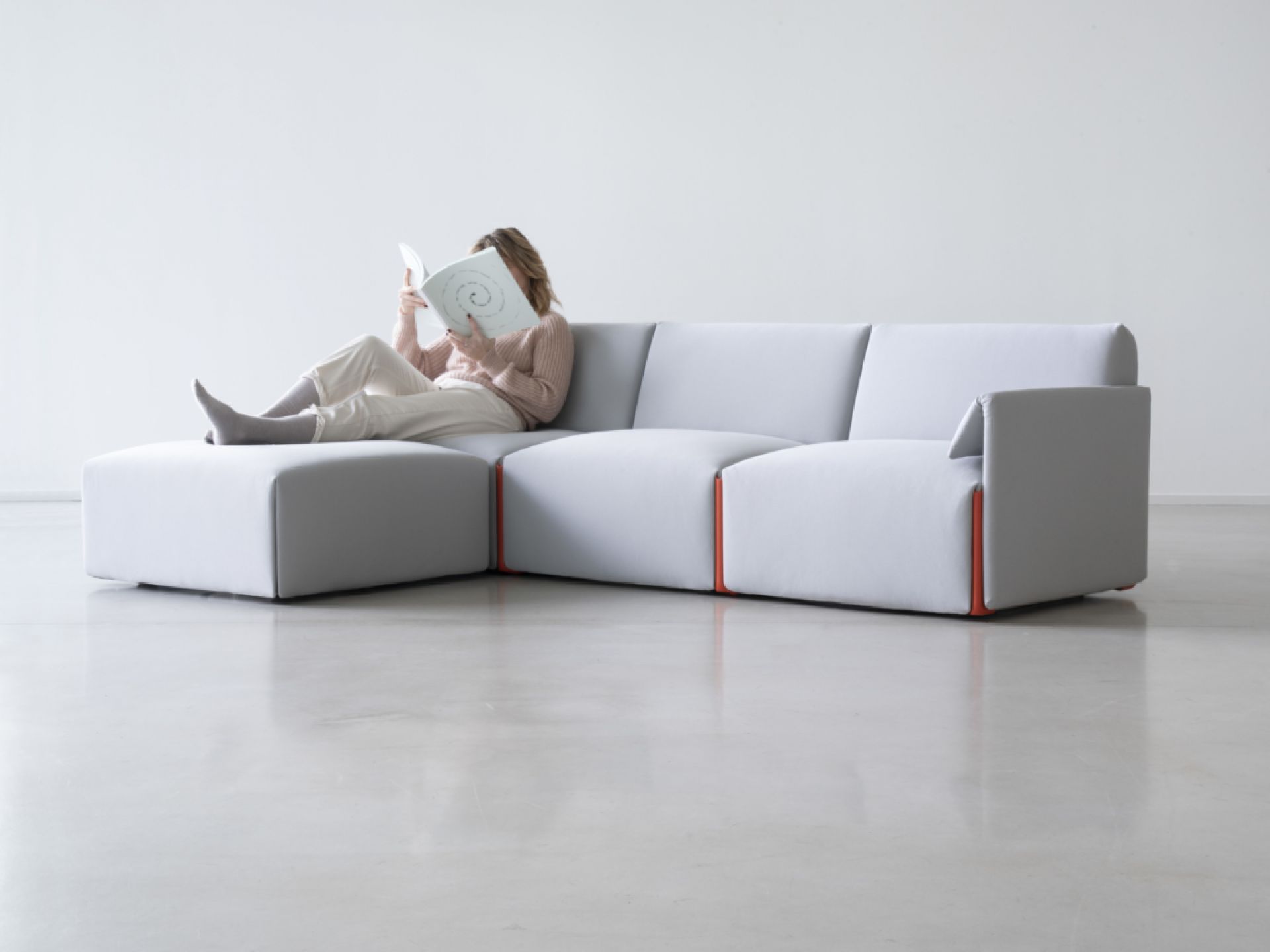 Costume Modulsofa mit Armlehne links, hellgrau mit orangen Akzenten, Frau liest Buch.
