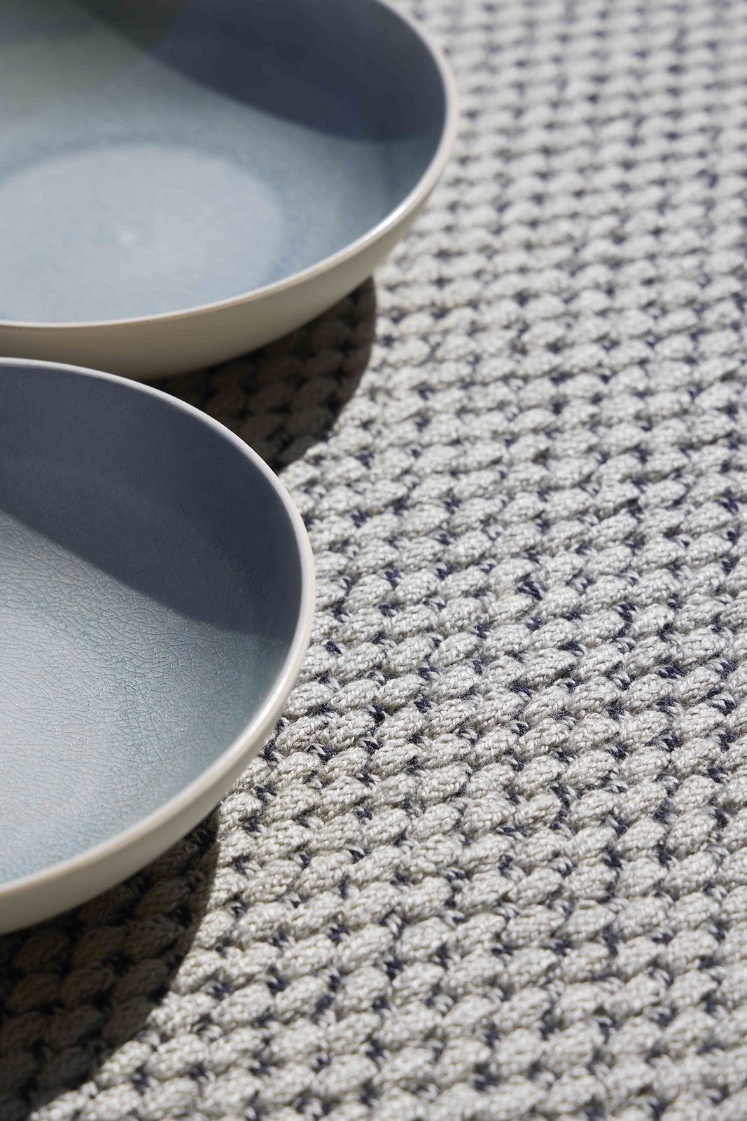 Detailaufnahme des Saline Outdoor Rug Teppichs von Gan mit zwei blauen Schalen.
