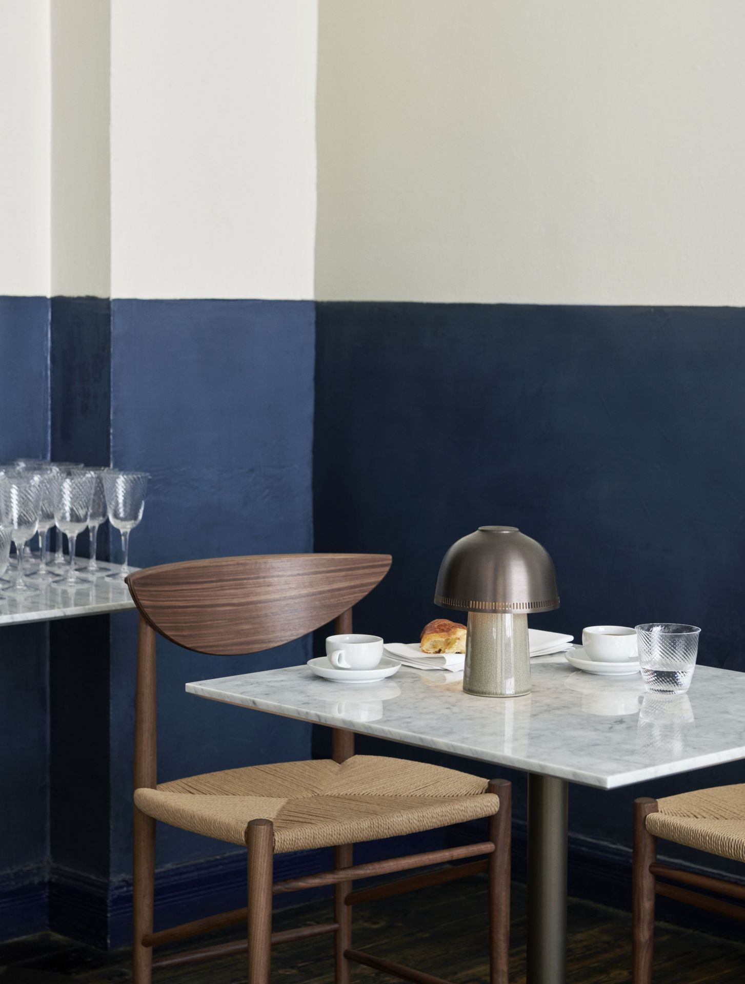 AndTradition Raku SH8 Akkuleuchte auf Marmortisch mit Stühlen, Tasse, Glas und Gebäck.