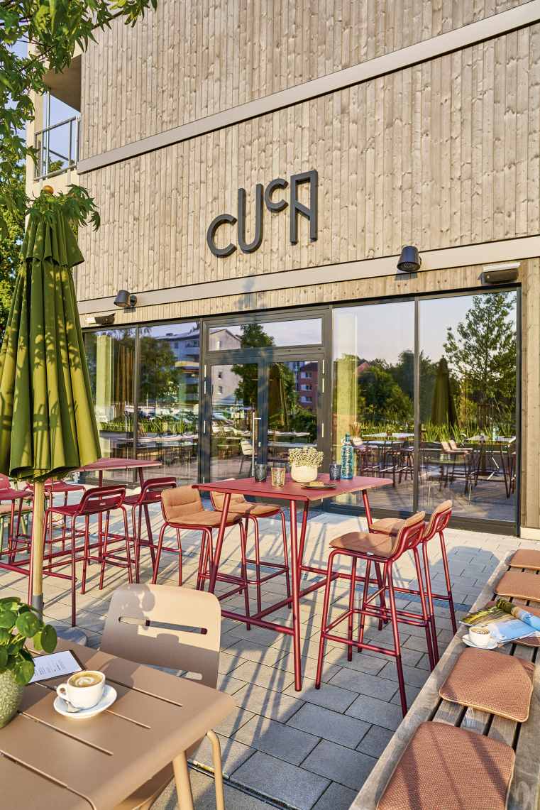 Außenbereich eines Cafés mit Weishäupl Vapio Sesseln und Tischen in Rot und Beige.