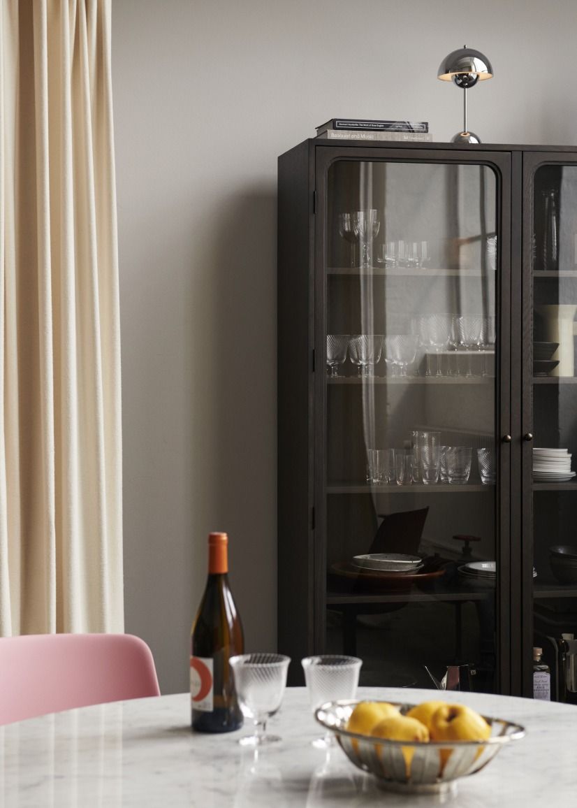 AndTradition Trace SC88 Vitrine aus dunklem Holz mit Glastüren, gefüllt mit Gläsern und Geschirr.