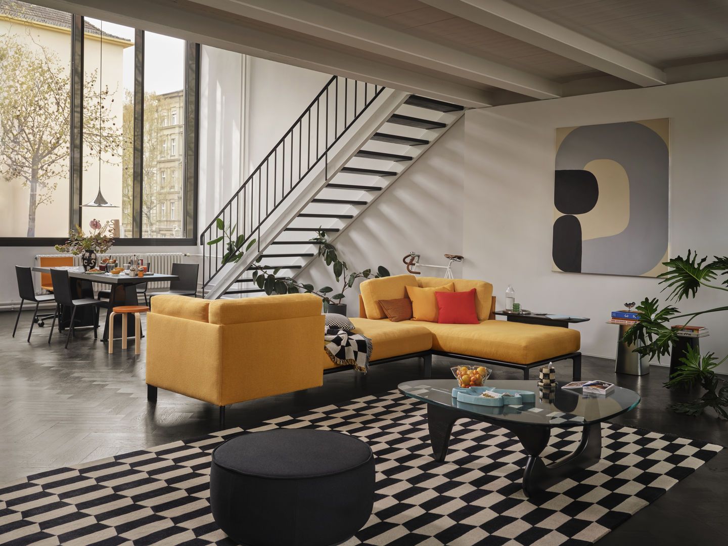 Wohnzimmer mit gelbem Sofa, Vitra Kissen, Teppichmuster, Treppe und Esstisch für modernes Wohnen.
