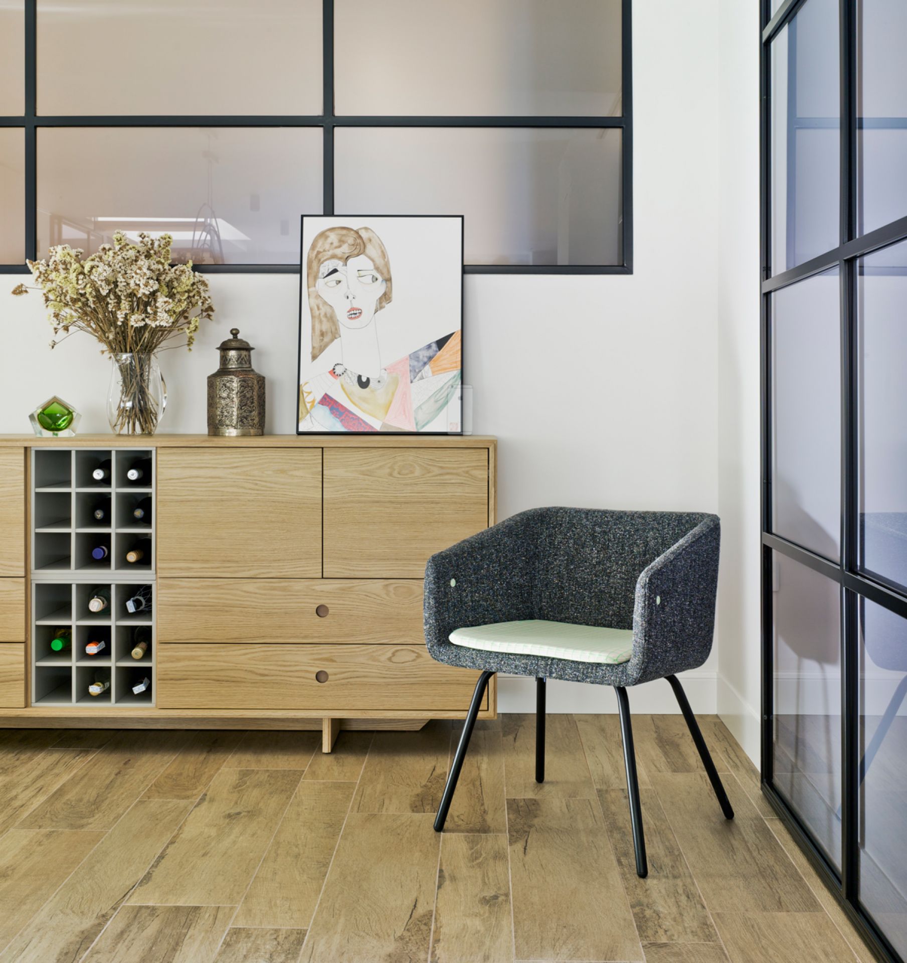 Grauer Sancal Collar Stuhl mit Armlehnen und schwarzem Gestell vor Sideboard. Designermöbel.