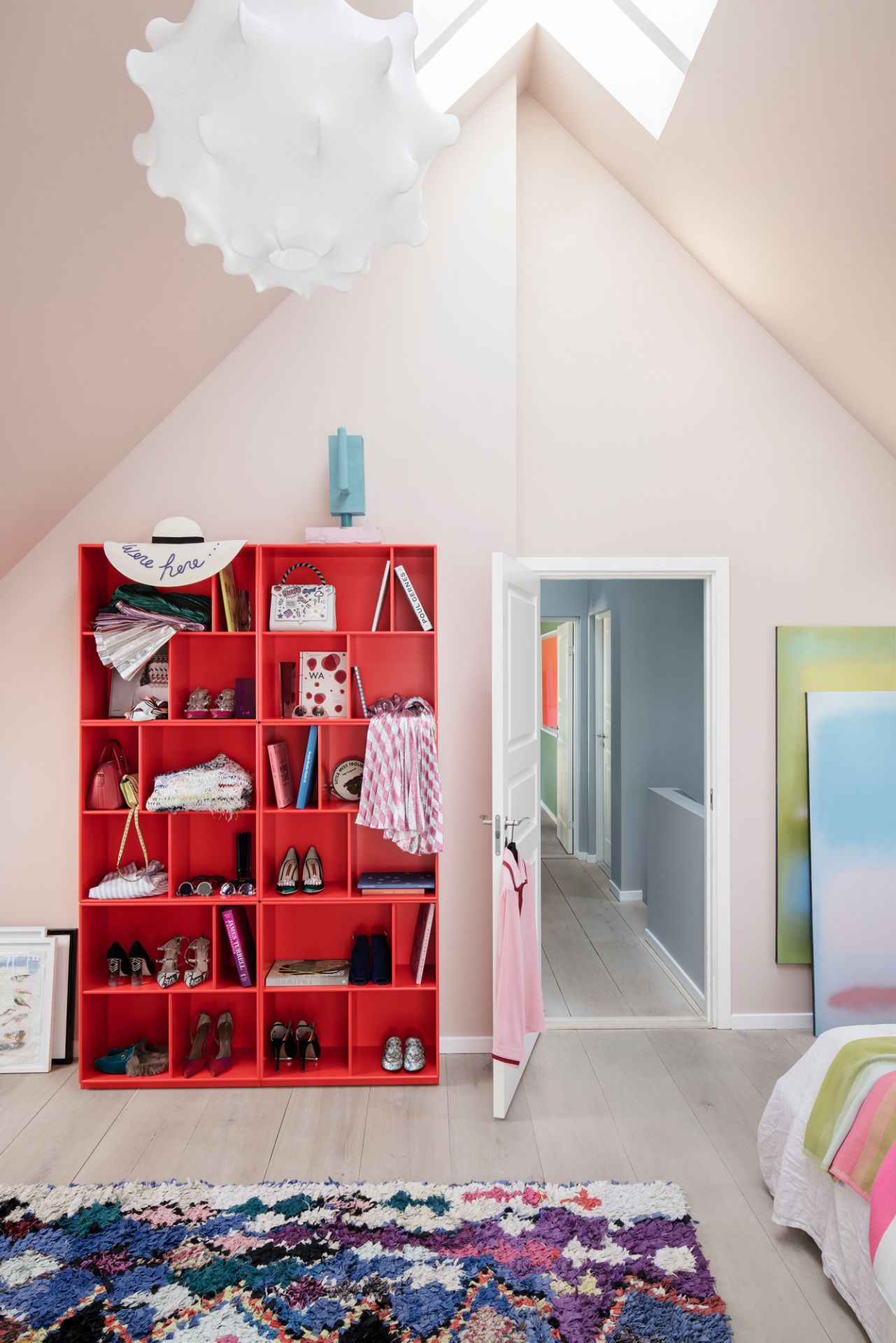 Rotes Montana Bücherregal im Dachgeschoss, gefüllt mit Büchern, Schuhen und Accessoires. Modernes Regaldesign.