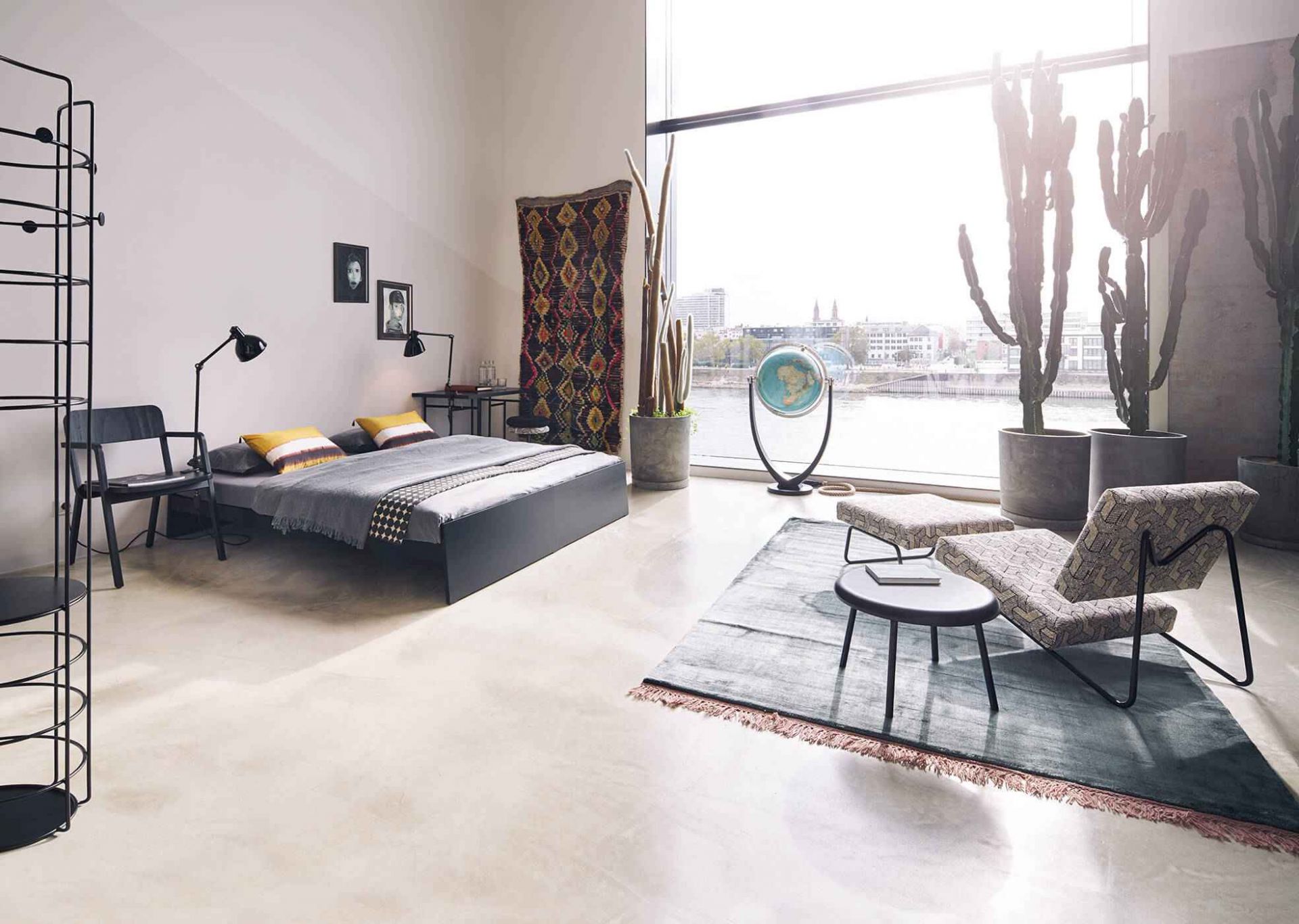 Schlafzimmer mit Lönneberga Bett, Stuhl, Teppich und großem Fenster mit Blick auf die Stadt.