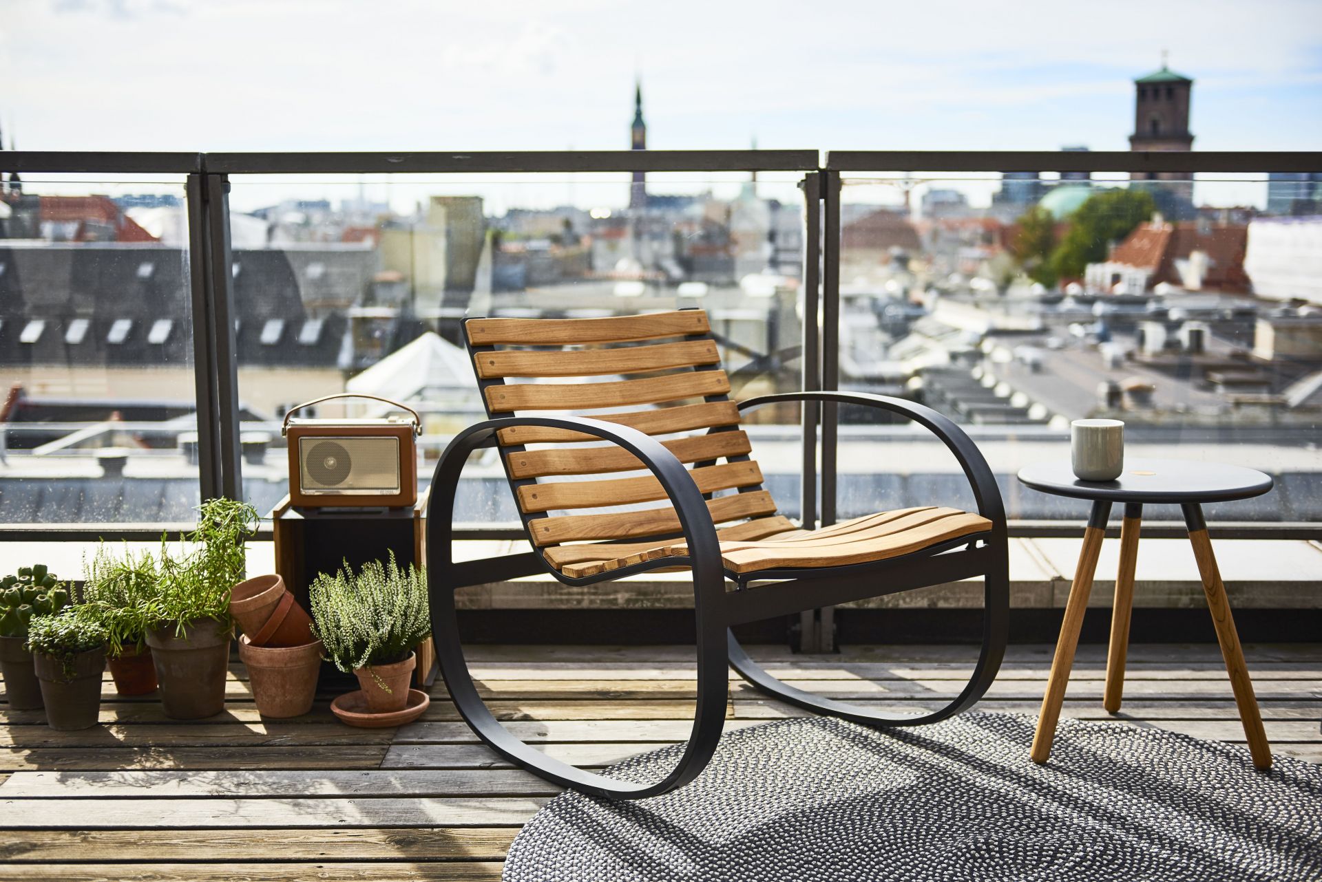 Parc Schaukelstuhl von Cane-Line auf einer Dachterrasse mit Blick auf die Stadt. Holz und Metall.