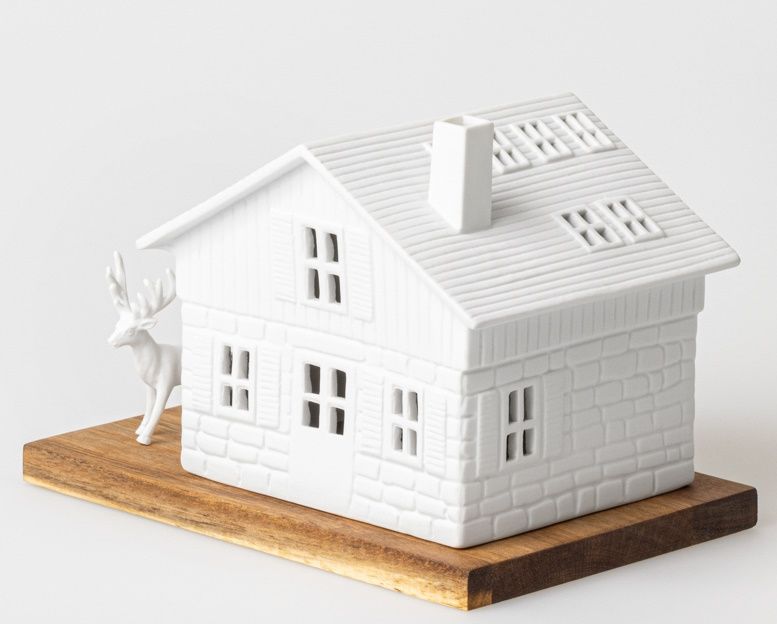 Lichthaus Skihütte Räder: Weißes Porzellanhaus mit Hirschfigur auf Holzsockel, stimmungsvolle Winterdekoration.