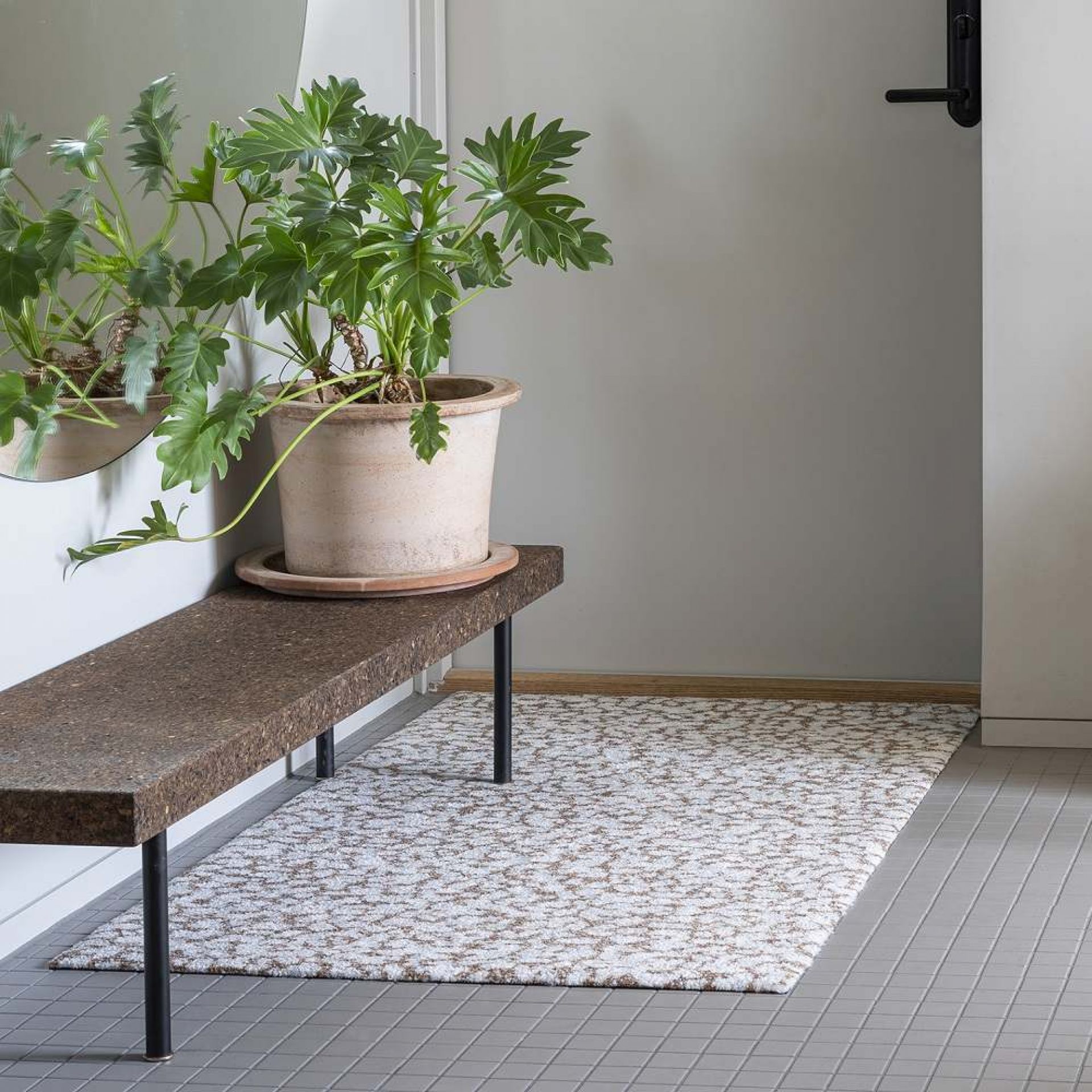 Heymat Fußmatte Grain Sandstone im Eingangsbereich, mit Bank und Pflanze dekoriert. Moderne, stilvolle Innenraum Fußmatte.