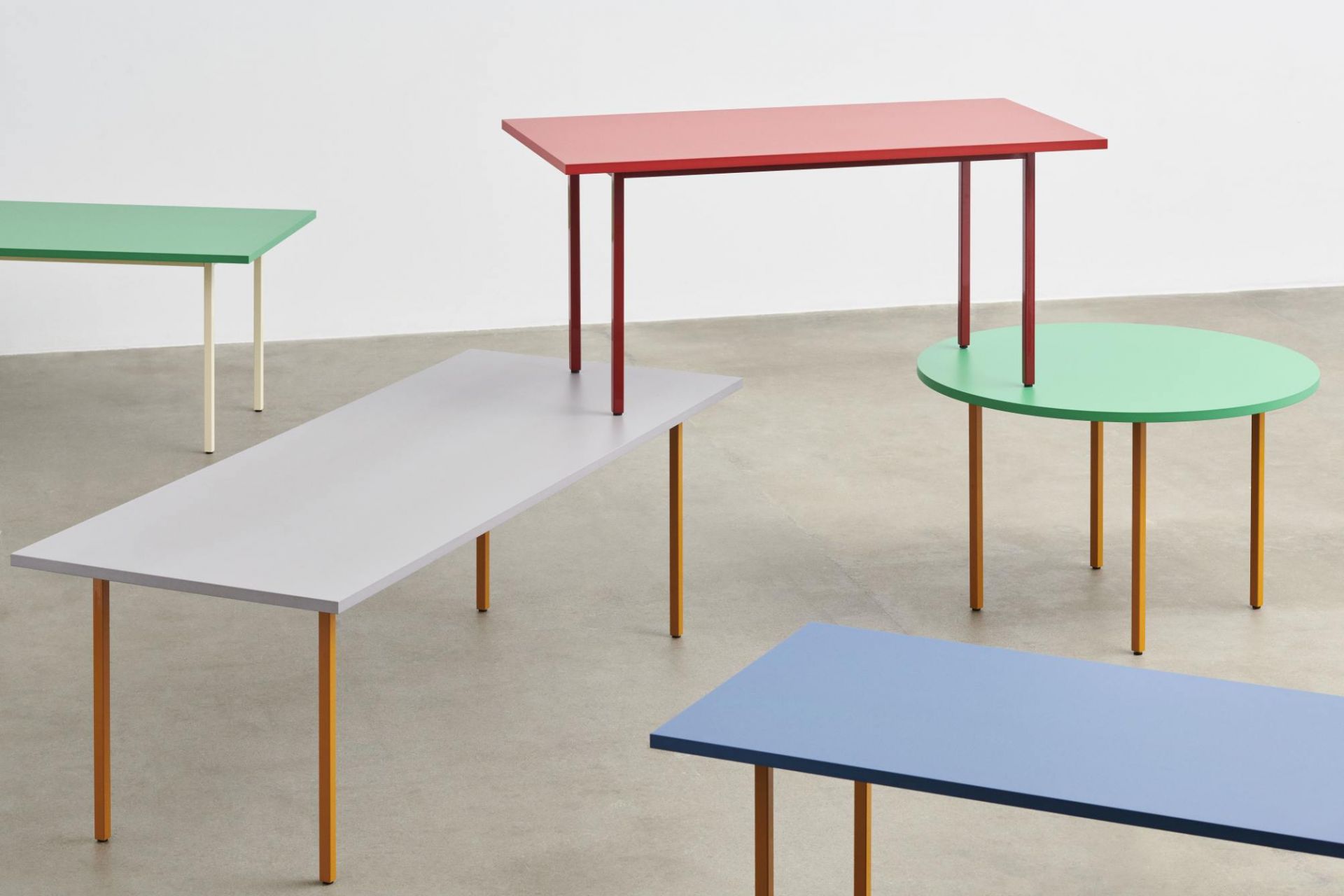 Mehrere farbige Tische der Two Colour Table Serie von Hay in verschiedenen Formen und Größen.