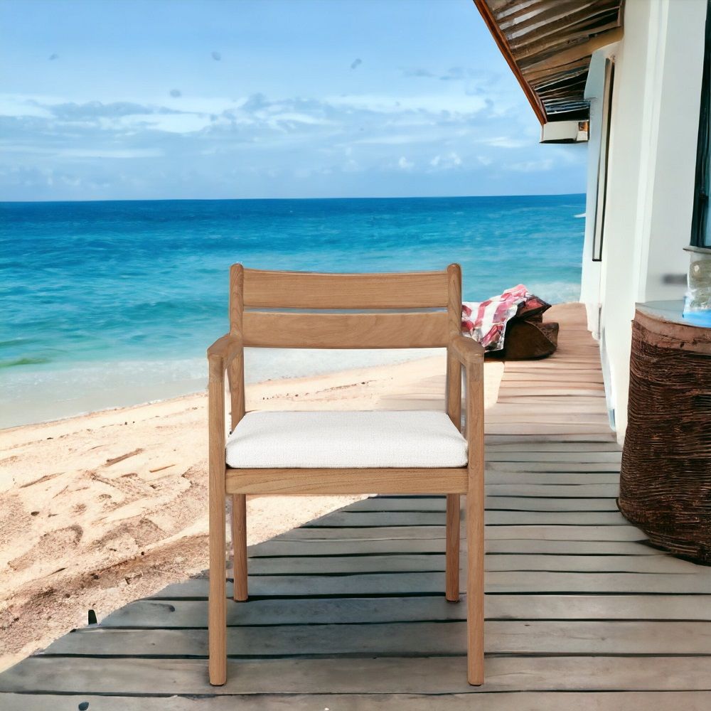 Jack Outdoor Stuhl aus Teakholz von Ethnicraft mit Armlehnen und weißem Sitzkissen auf Terrasse.