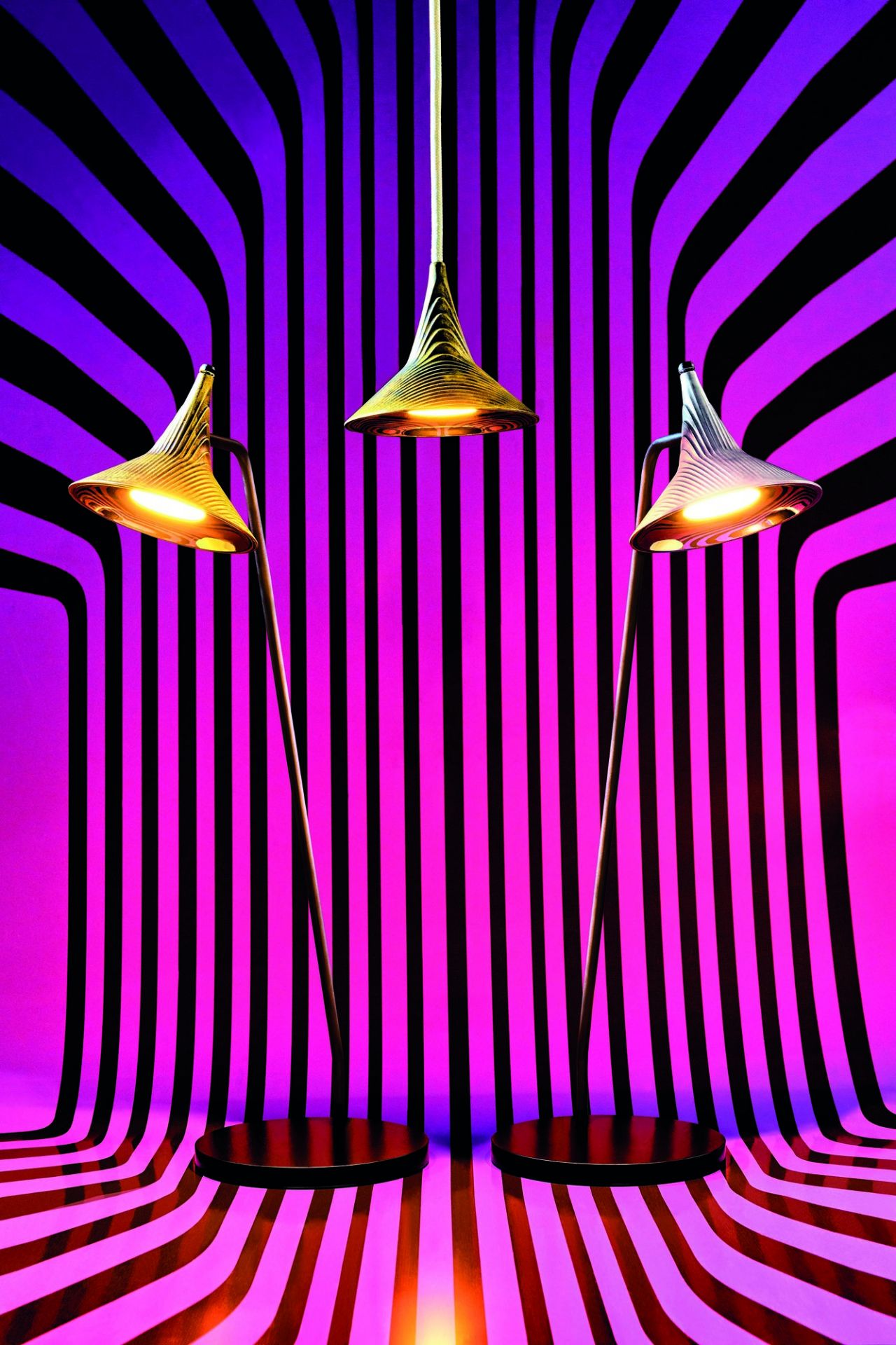 Drei Artemide Unterlinden Tischleuchten vor einem gestreiften, farbigen Hintergrund, moderne Innenbeleuchtung.