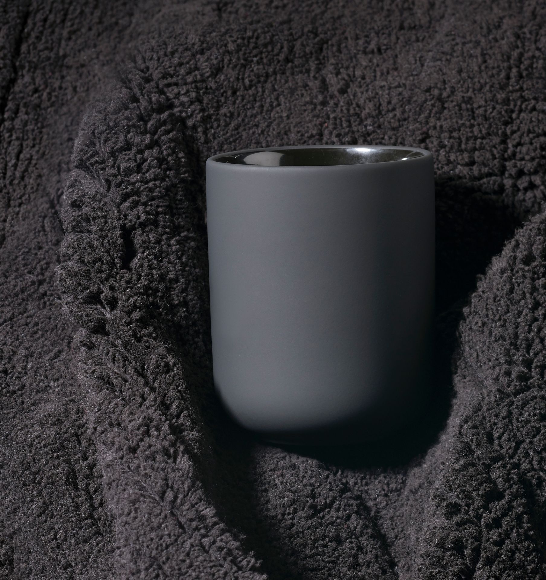 Grauer Ume Zahnputzbecher von Zone Denmark auf dunklem, strukturiertem Stoff für Badezimmeraccessoires und moderne Badgestaltung.