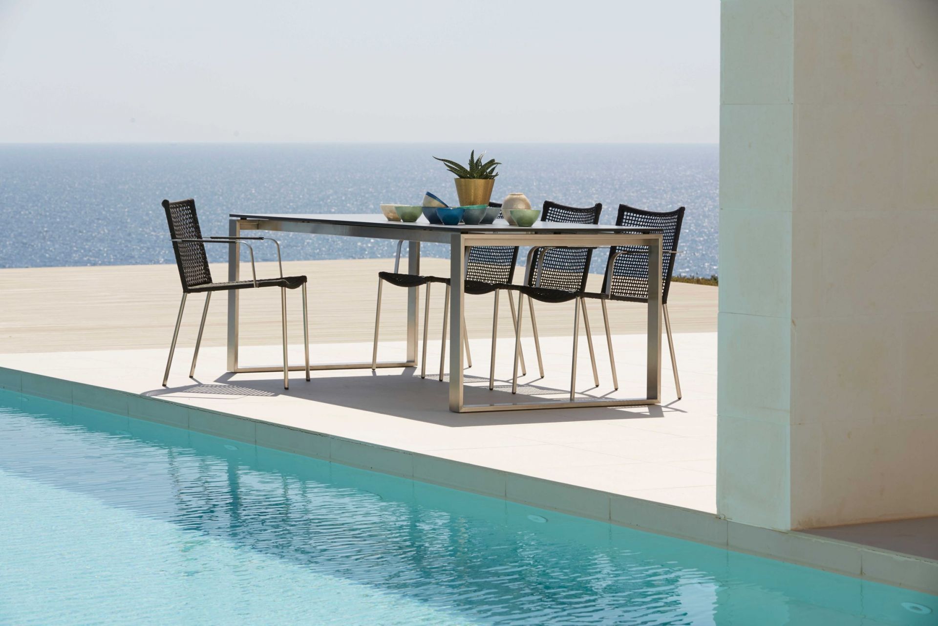 Cane-Line Straw Armlehnstuhl: Schwarzer Outdoor Stuhl aus Rattan mit Armlehnen am Pool.