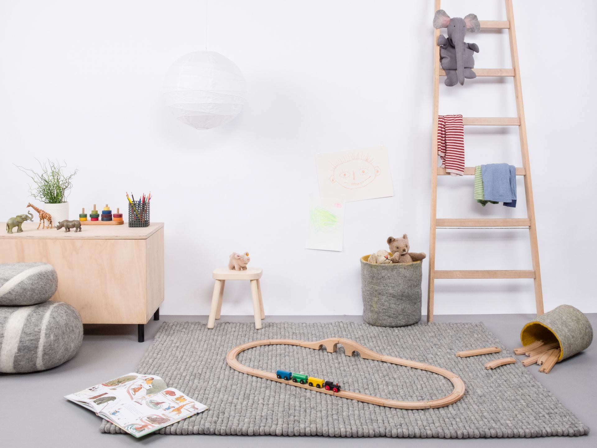 Grauer Filzkugel Teppich 160x230 cm im Kinderzimmer mit Spielzeug und Holzeisenbahn.