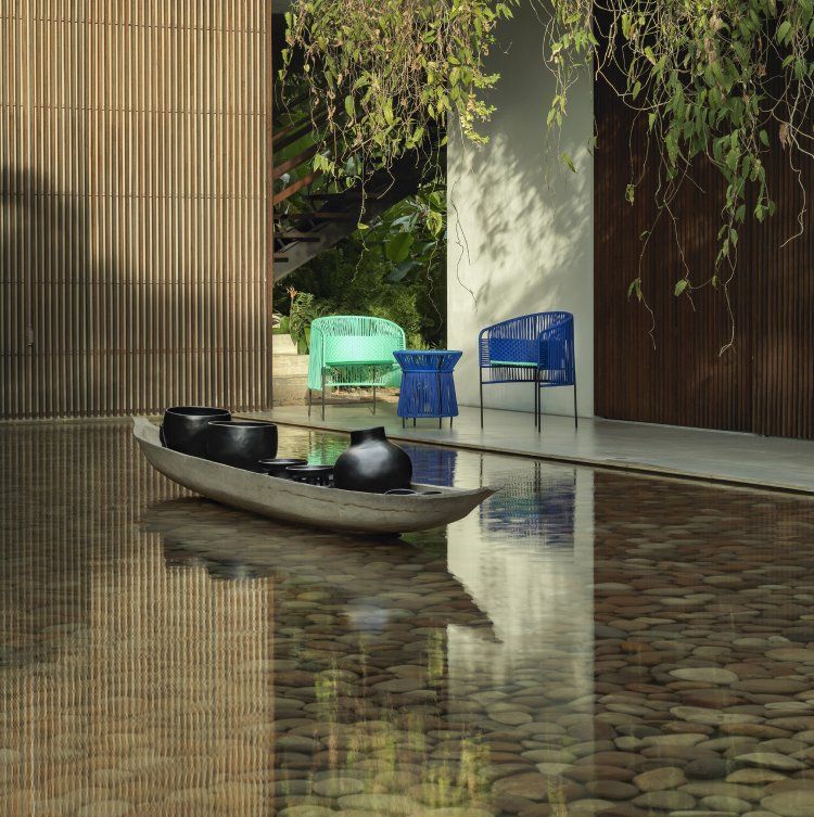 Caribe Dining Chair Outdoor: Türkis- und smaragdgrüne Gartenstühle neben einem Wasserbecken mit Steinen.