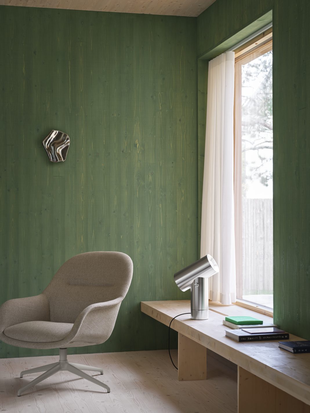 Muuto Beam Lamp Tischleuchte aus poliertem Aluminium auf einem Holztisch neben einem Fenster.