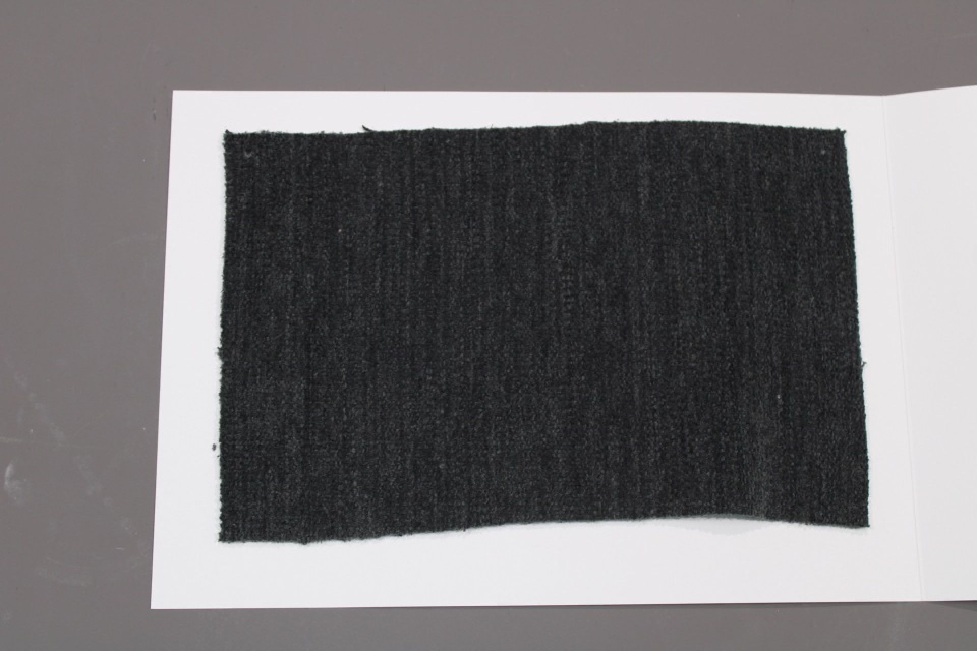 Stoffmusterkarte Gruppe 81 Cor: Nahaufnahme eines dunkelgrauen, gewebten Stoffmusters auf weißem Karton.