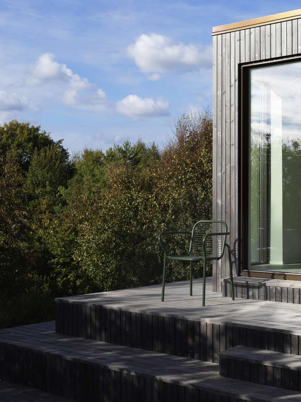 Grüner Vig Armchair Armlehnstuhl von Normann Copenhagen auf einer Holzterrasse vor einem modernen Haus.