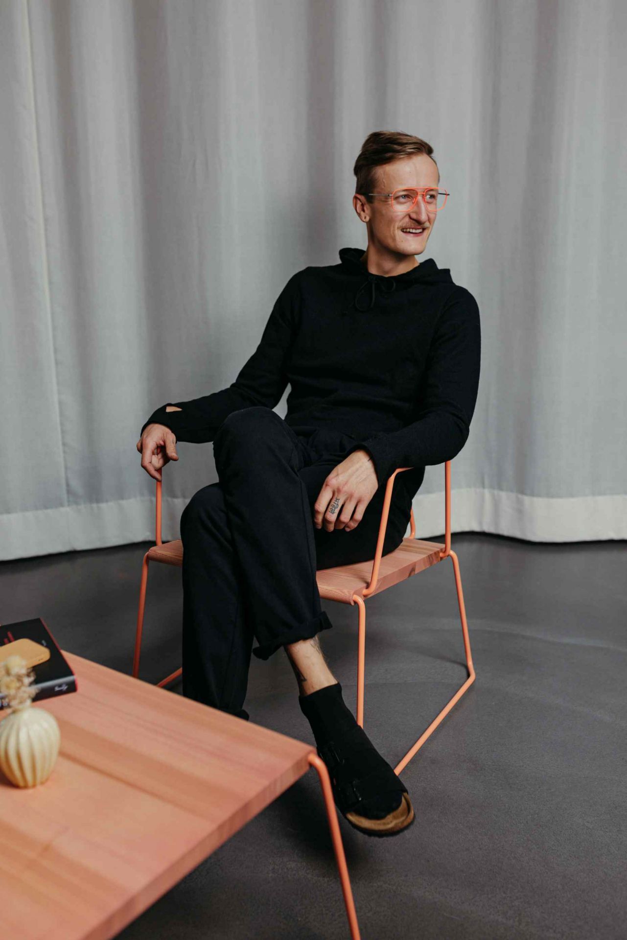 Mann sitzt auf einem Stuhl neben dem D:009 Coffeetable Kohleschwarz von Fuchs & Habicht.