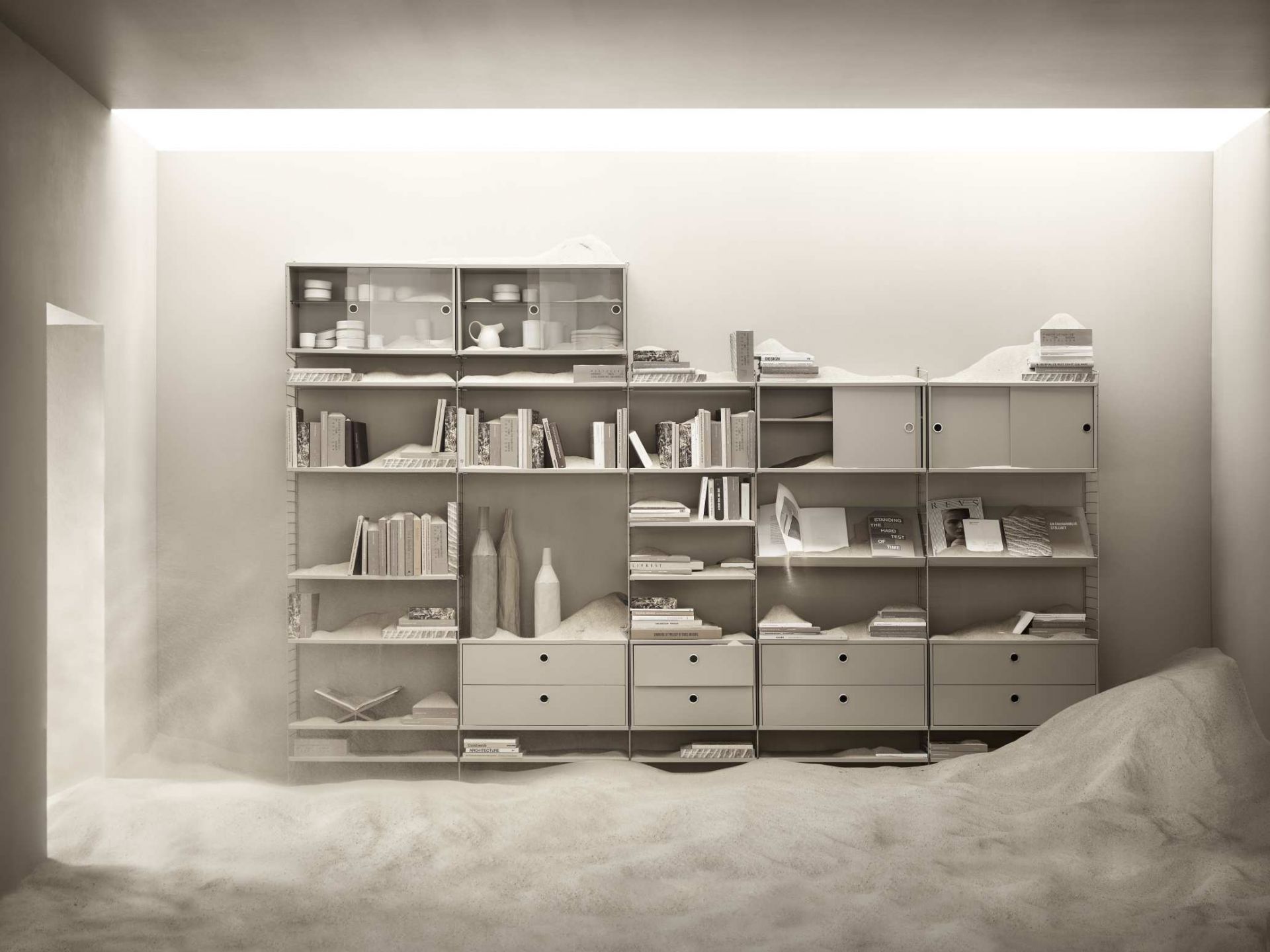 Graues String Regal mit Schränken, Schubladen und Regalböden, dekoriert mit Büchern und Vasen.