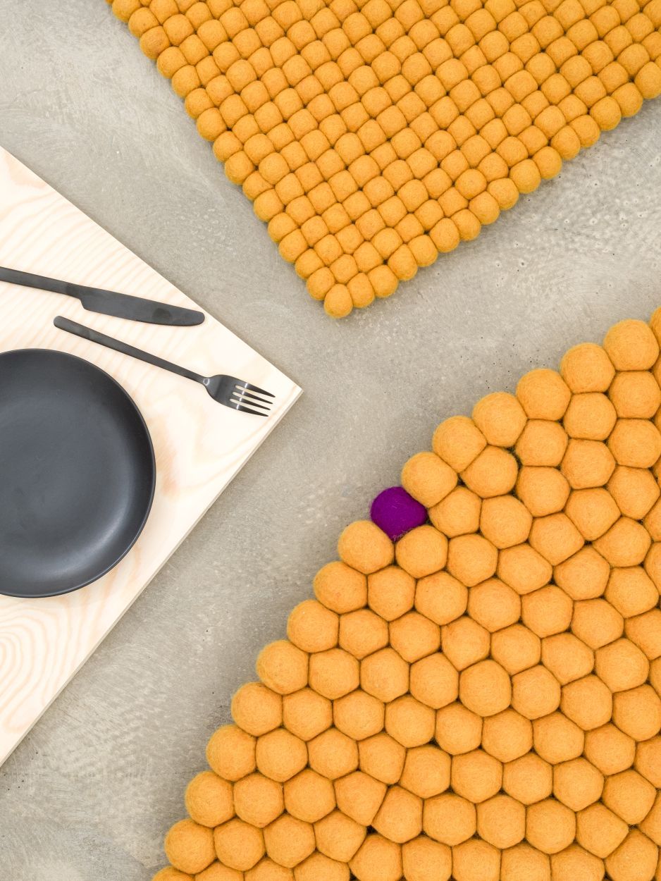 Ockergelber myfelt Filzteppich "Big One" aus runden Filzkugeln, Detailaufnahme mit Teller und Besteck.