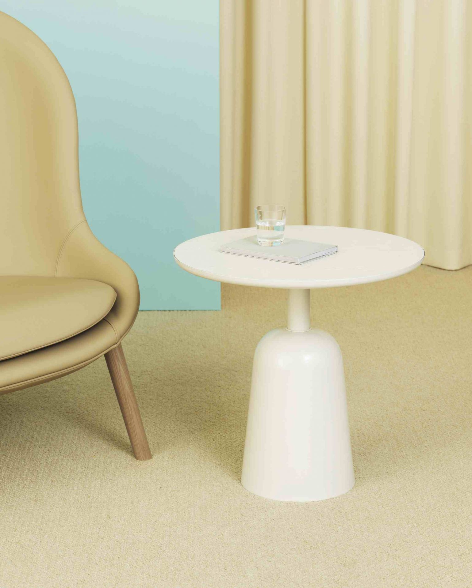 Weißer Turn Table Beistelltisch von Normann Copenhagen neben beigem Sessel mit Glas Wasser.
