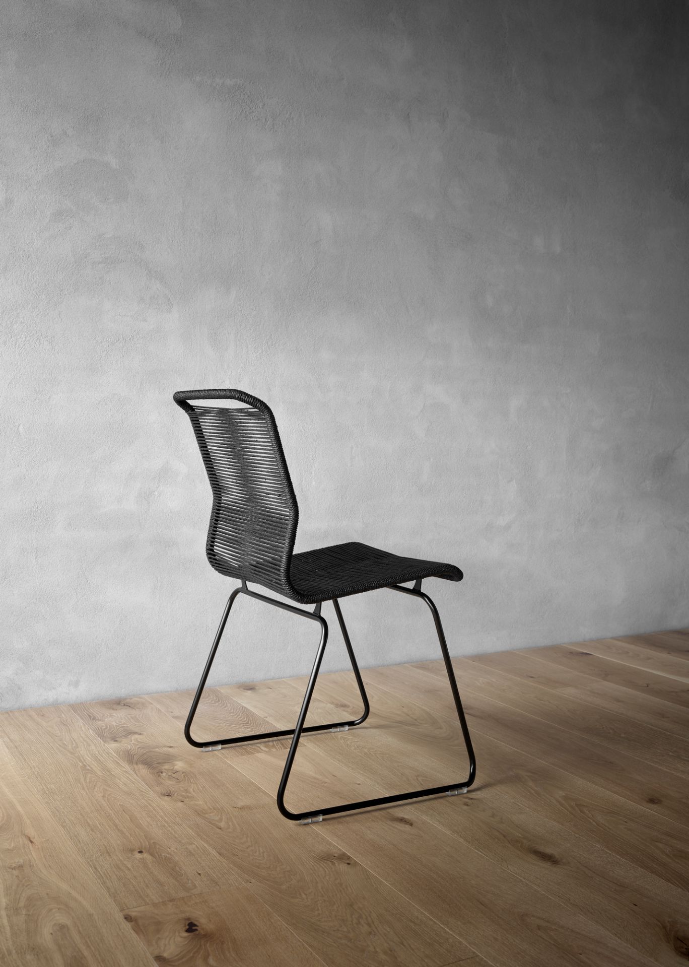 Schwarzer Panton One Stuhl mit Kordelbespannung und schwarzem Metallgestell auf hellem Holzboden. Design Stuhl.