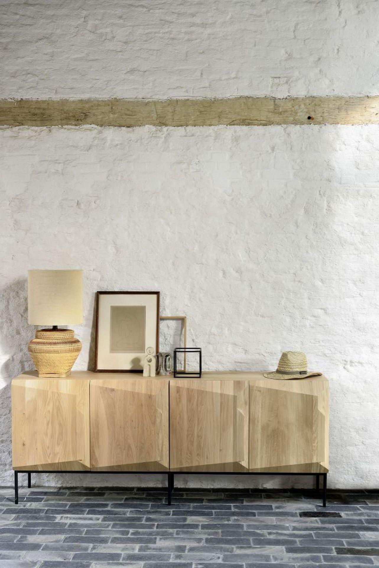 Ethnicraft Stairs Anrichte aus Eiche mit vier Türen und schwarzem Metallgestell vor weißer Wand.