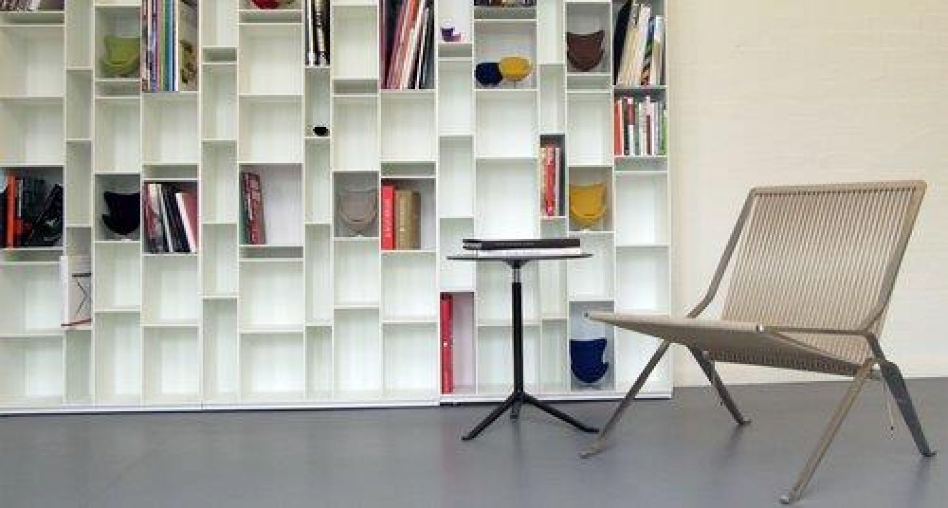 Beiger PK25 Sessel von Fritz Hansen mit minimalistischem Design und Stahlgestell vor Bücherregal.