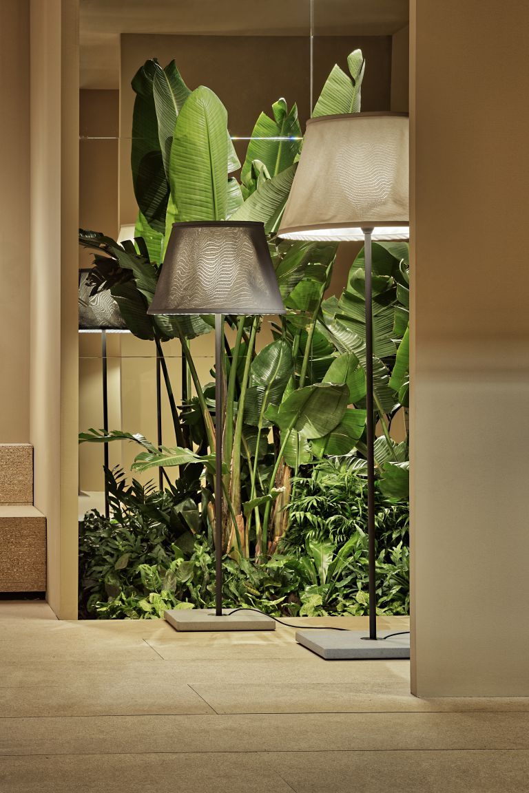 Beige TXL Stehleuchte von Marset, eine moderne Outdoor-Lampe mit Textilschirm vor üppigem Grün.