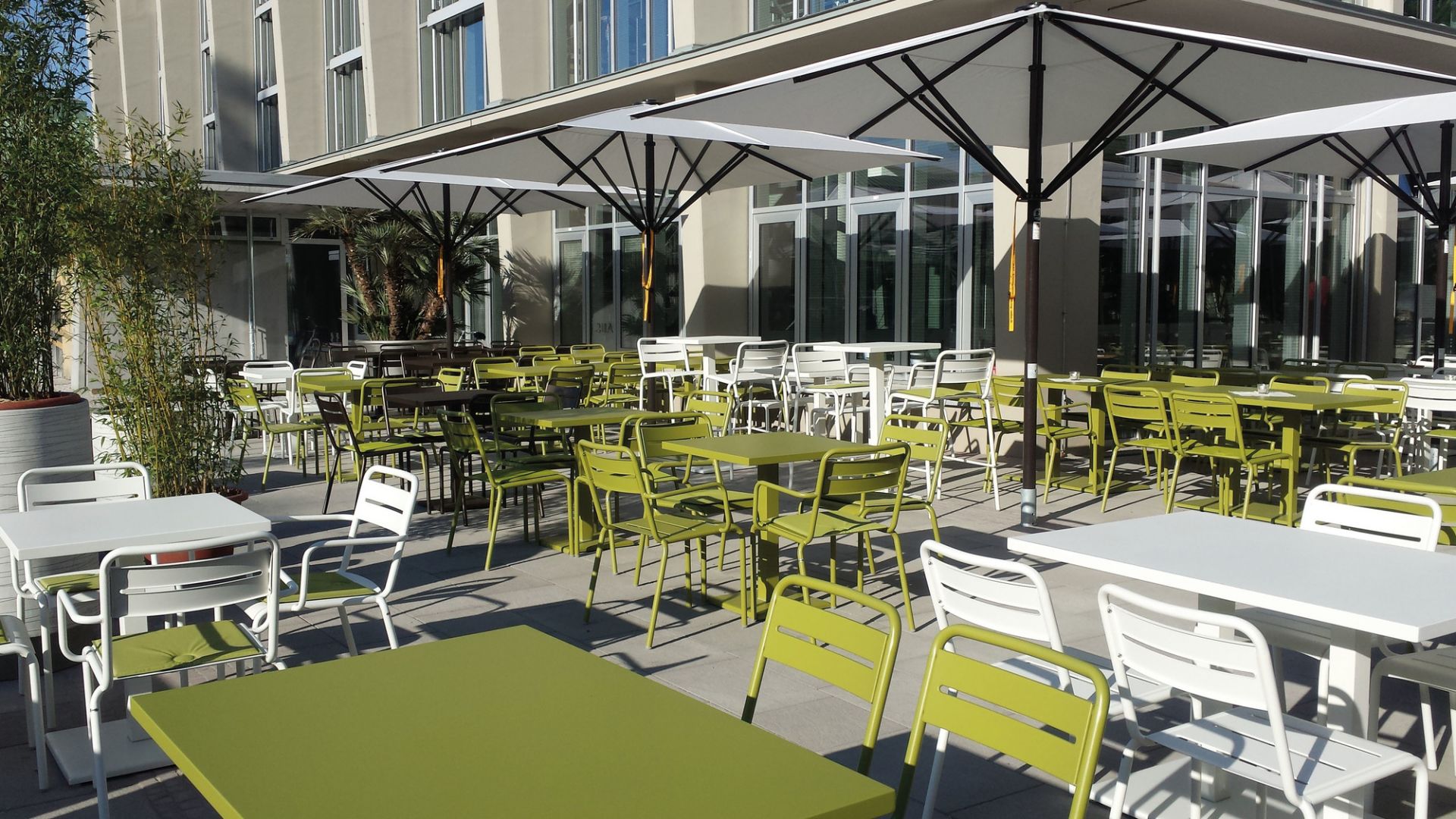 Außenbereich mit grünen Emu Star Armlehnstühlen und weißen Tischen unter Sonnenschirmen.
