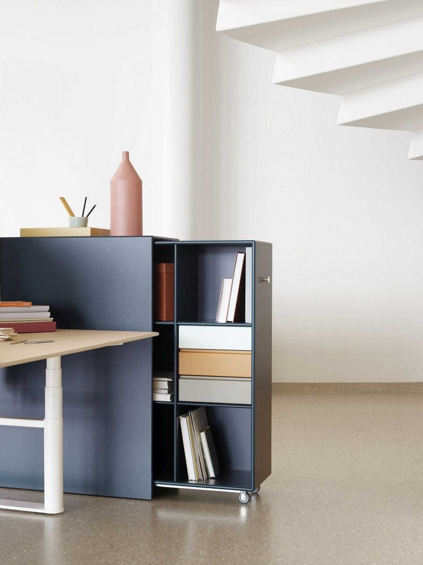 HiLow höhenverstellbarer Arbeitstisch von Montana mit blauem Sideboard und Rollcontainer für Büroorganisation.