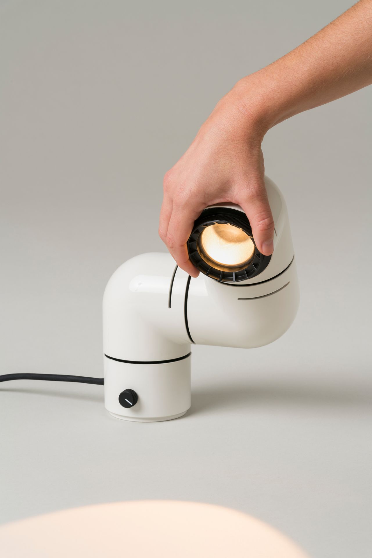 Nahaufnahme der weißen Tatu Tischleuchte von Santa & Cole, die von einer Hand gehalten wird.
