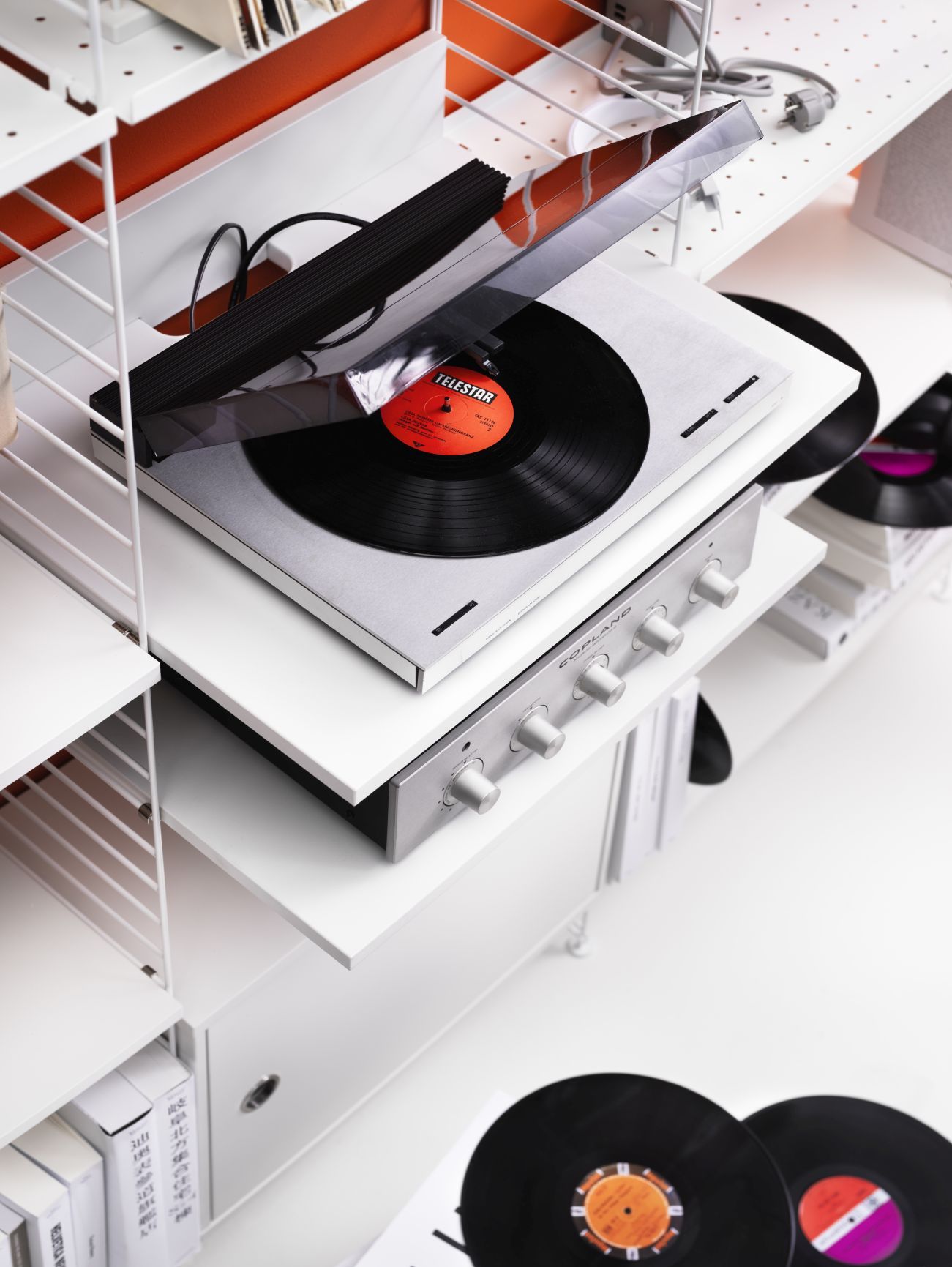 Detailaufnahme eines weißen String Regalsystems mit Schallplattenspieler und Verstärker. Ideal für Wohnzimmer und Musikliebhaber.