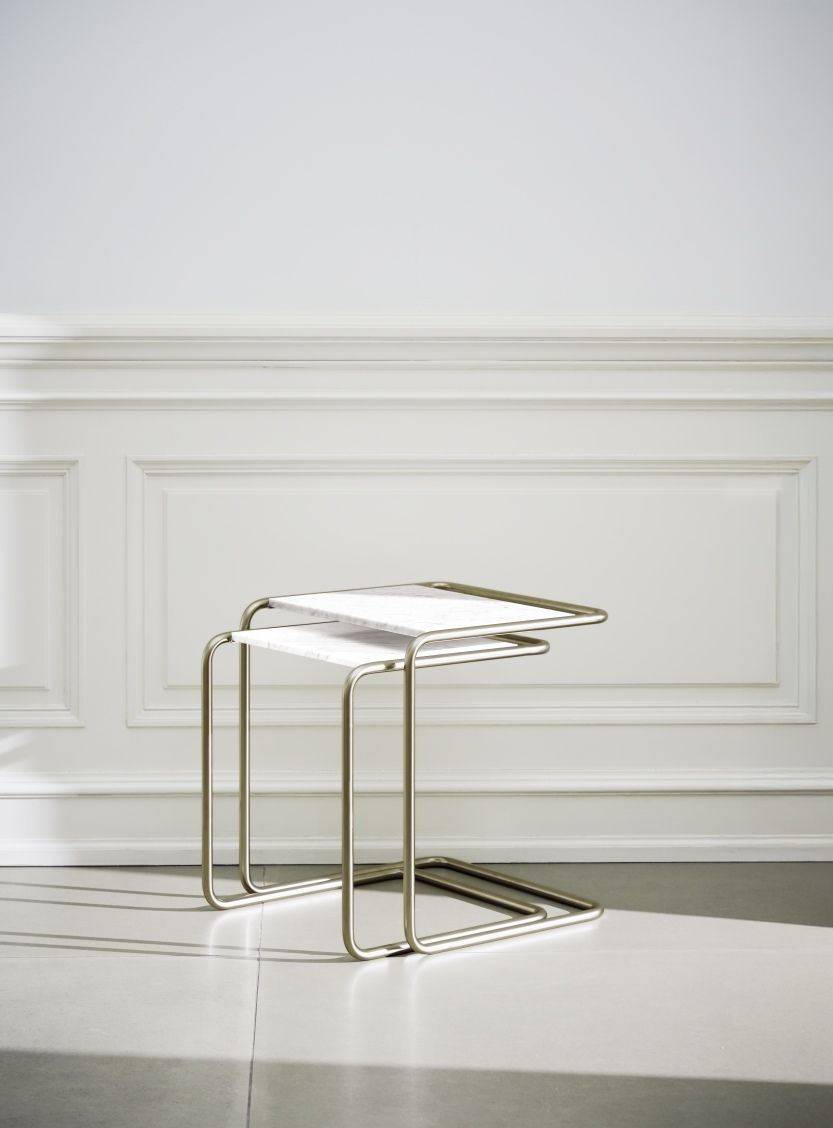 JS. Thonet B97 Beistelltisch: Zwei goldfarbene, minimalistische Tische mit Marmorplatte vor weißer Wand.