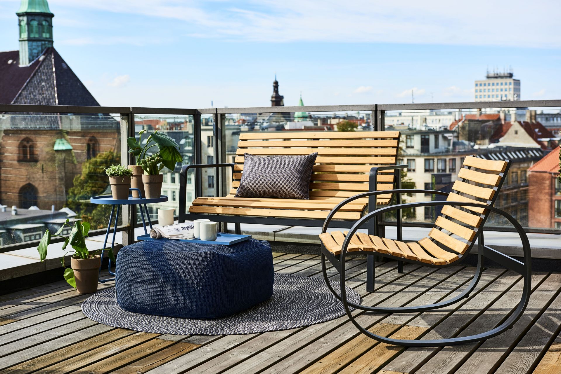 Parc Schaukelstuhl von Cane-Line aus Teakholz und Metall auf einer Dachterrasse mit Stadtblick.
