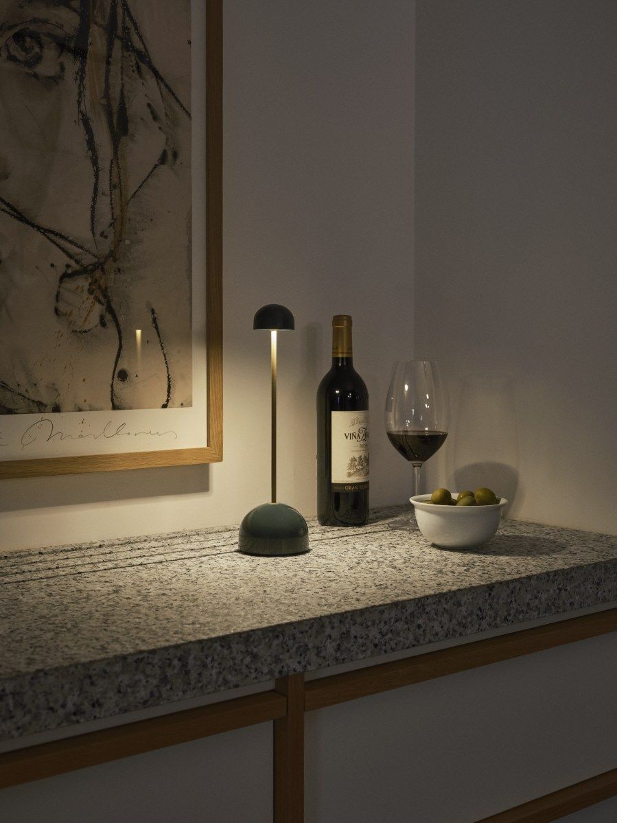 Sips Akkuleuchte von Marset, weiße Tischleuchte mit silbernem Ständer neben Wein und Oliven.