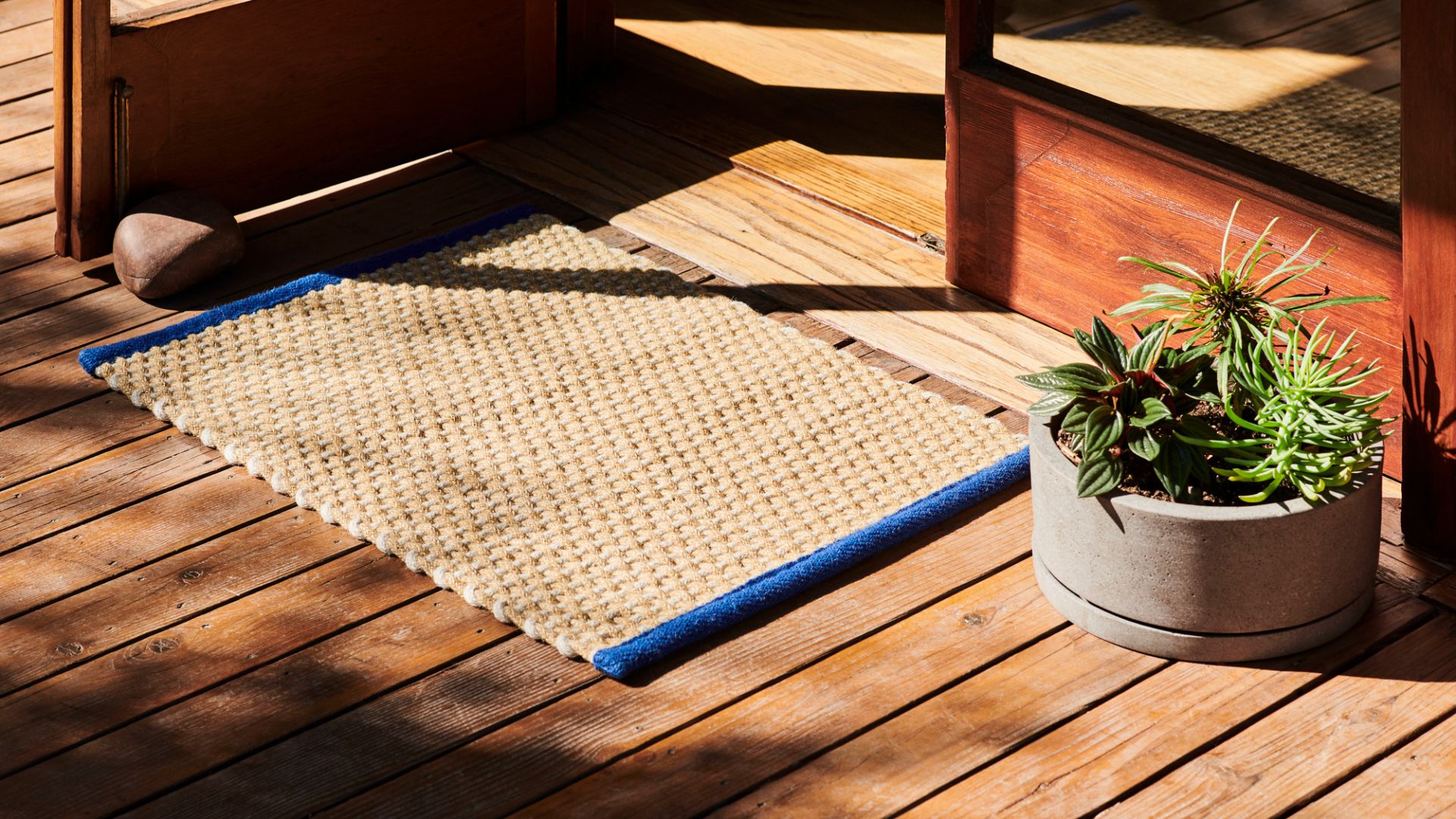 Beiger Hay Teppich mit blauem Rand vor einer Holztür, ideal als Fußmatte.