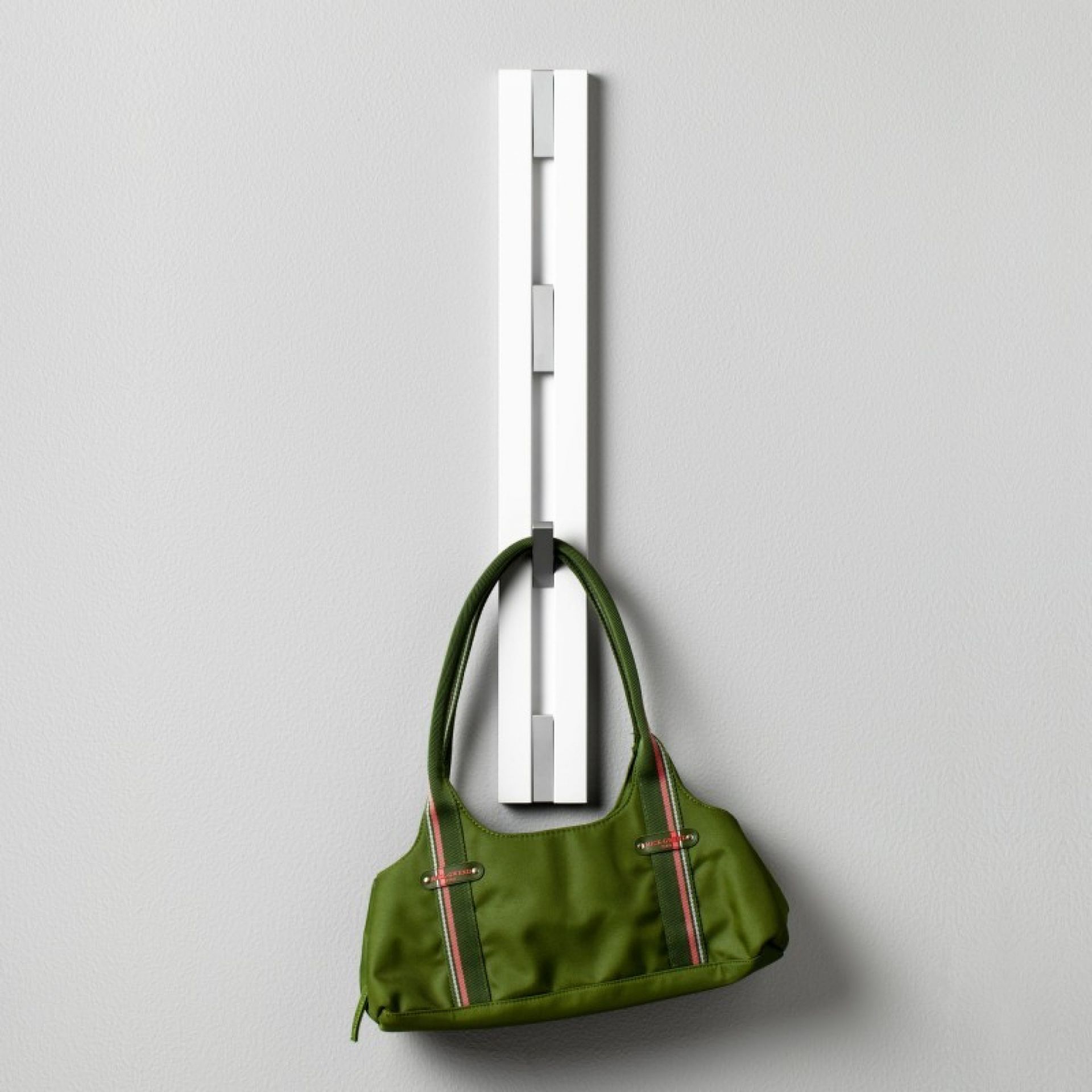 Weiße Knax Wandgarderobe mit vier Haken, daran hängt eine grüne Handtasche. Vertikale Garderobenleiste.