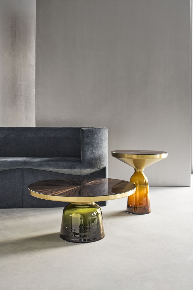 Bell Side Table von ClassiCon mit Tischplatte in Strohmarketerie und farbigem Glasfuß neben Sofa.