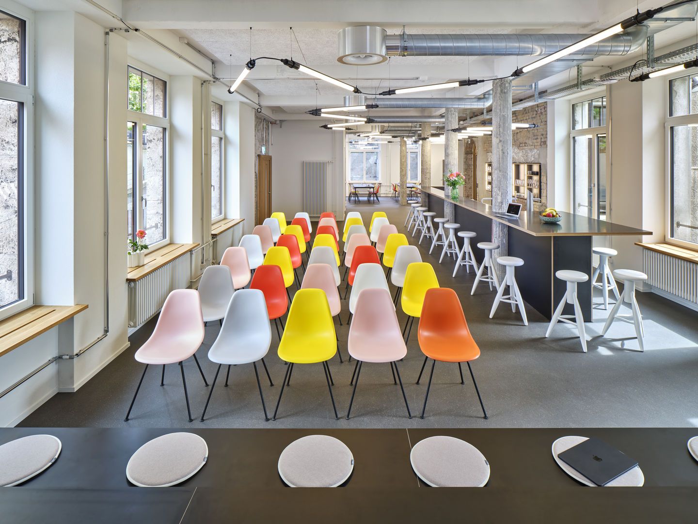 Raum mit vielen bunten Eames Plastic Chairs von Vitra, ideal für Konferenzen und Meetings.