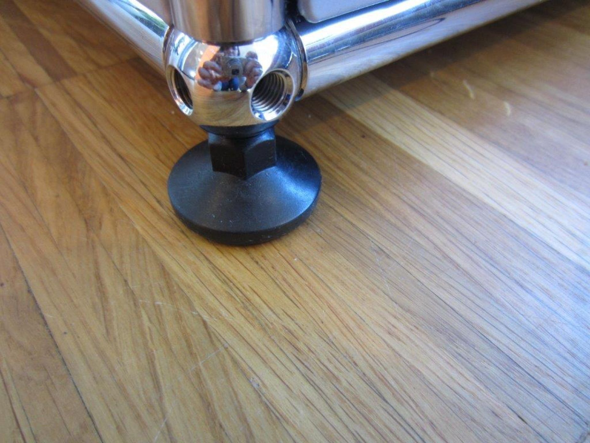 Nahaufnahme eines USM Haller Möbelfußes / Nivellierfußes als Ersatzteil, mit Chromkugel und schwarzem Fuß auf Holzboden.
