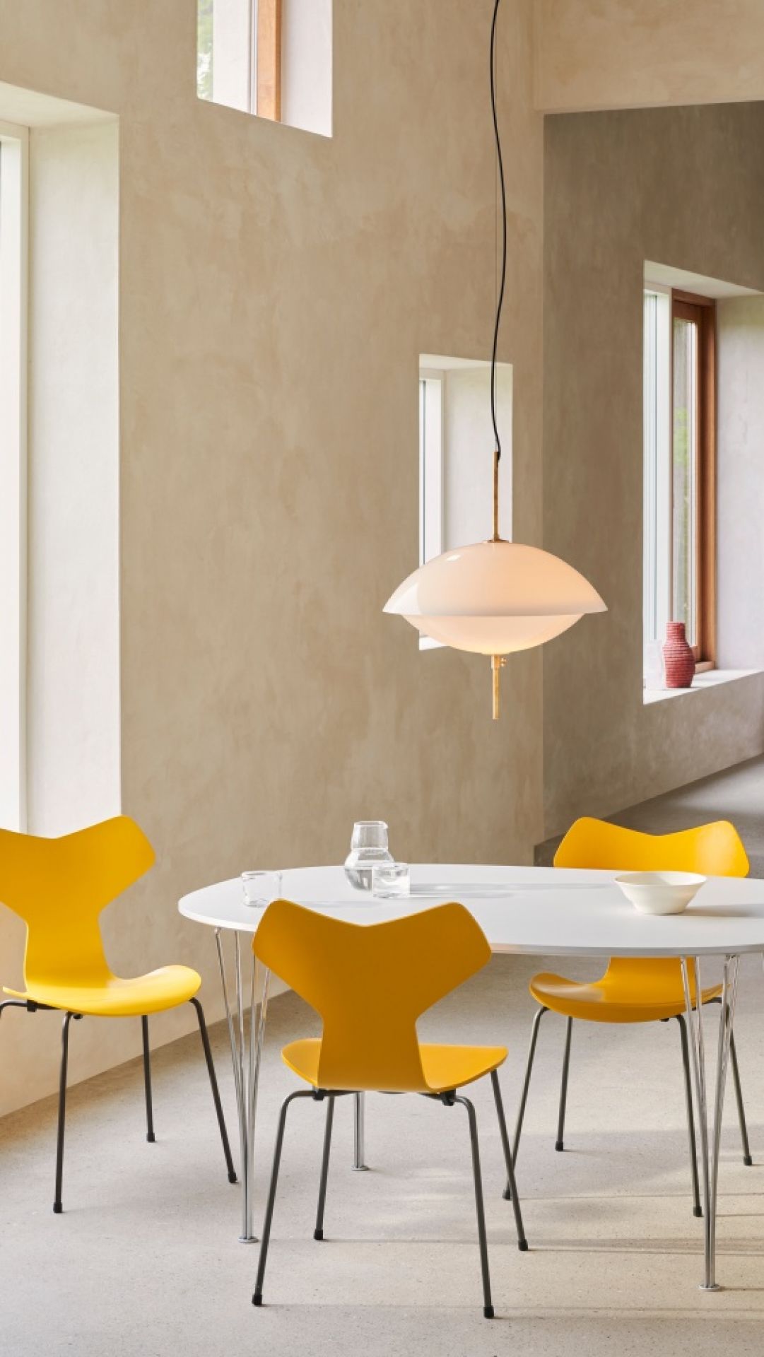 Helle Clam Pendelleuchte von Fritz Hansen über einem Esstisch mit gelben Stühlen.